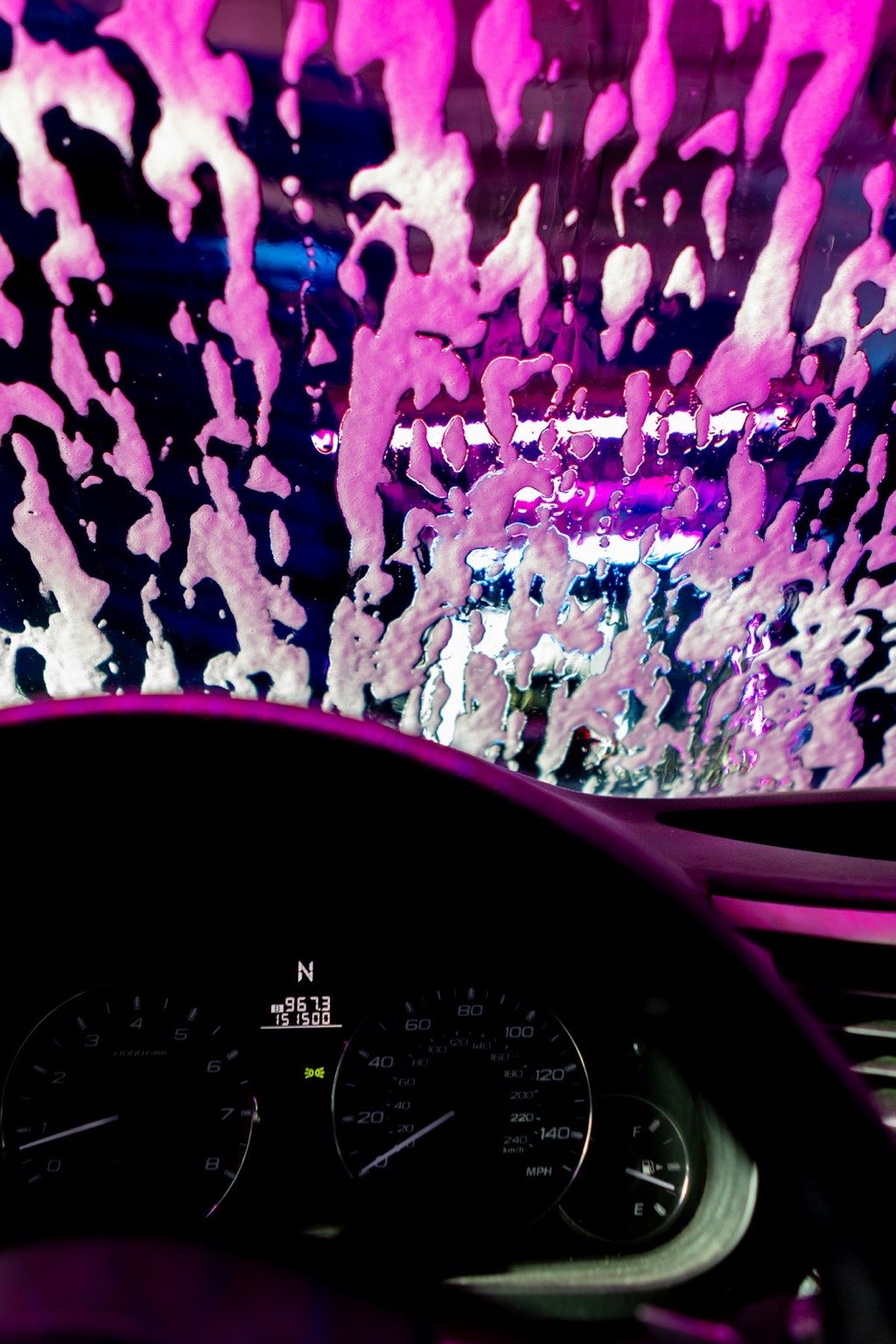 Driver's view through a windshield covered in pink and violet foam inside the car wash tunnel